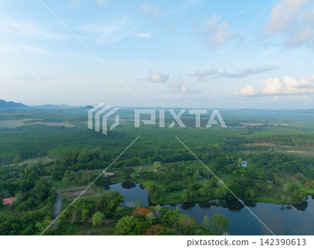 Aerial view of tranquil lake within tropical retreat resort surrounded by lush forest and distant mountains. Peaceful nature escape for wellness travel and relaxation. Wellness and nature tourism. Aerial view of tranquil lake within tropical retreat resort surrounded by lush forest and distant mountains. Peaceful nature escape for wellness travel and relaxation. Wellness and nature tourism. 142390613