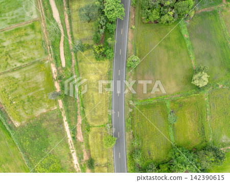 Top down aerial view of quiet country road running through patchwork agricultural fields and lush vegetation. Rural transportation, farming landscape and land use development. Transport infrastructure Top down aerial view of quiet country road running through patchwork agricultural fields and lush vegetation. Rural transportation, farming landscape and land use development. Transport infrastructure 142390615
