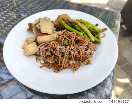 Savory Indonesian stir-fried noodles (mie goreng) served with green vegetables and tofu on a white ceramic plate Savory Indonesian stir-fried noodles (mie goreng) served with green vegetables and tofu on a white ceramic plate 142391117