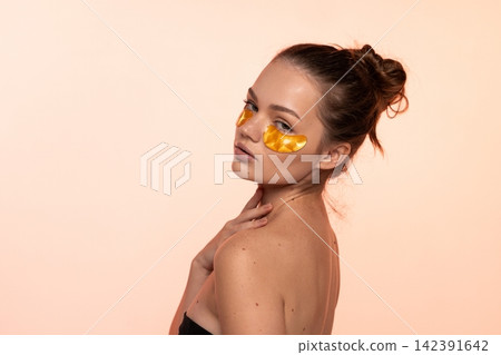 Young woman applying golden undereye patches, focusing on beauty, skincare, and facial treatment with a clean aesthetic Young woman applying golden undereye patches, focusing on beauty, skincare, and facial treatment with a clean aesthetic 142391642
