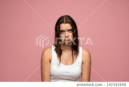 Young woman feeling upset and showing disappointment with a pout, modeling emotions on a pink background Young woman feeling upset and showing disappointment with a pout, modeling emotions on a pink background 142391648