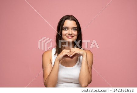 Young woman making heart gesture with hands, expressing love, joy, and kindness on pink background Young woman making heart gesture with hands, expressing love, joy, and kindness on pink background 142391658