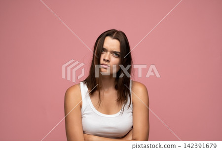 Woman expressing annoyance and disbelief, arms crossed, feeling upset and skeptical against a pink background 142391679