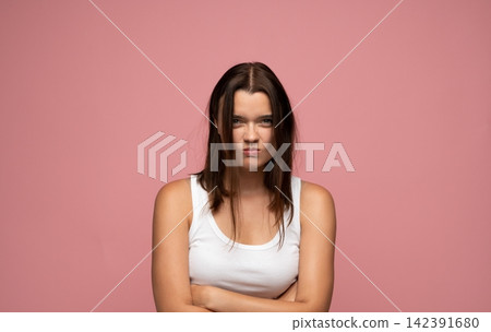 Woman pouting with crossed arms, feeling grumpy and frustrated against a pink background, expressing annoyance and negative emotions Woman pouting with crossed arms, feeling grumpy and frustrated against a pink background, expressing annoyance and negative emotions 142391680