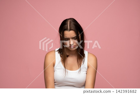 Young woman feeling sad and depressed, experiencing emotional stress and mental health issues, looking down on a pink background 142391682