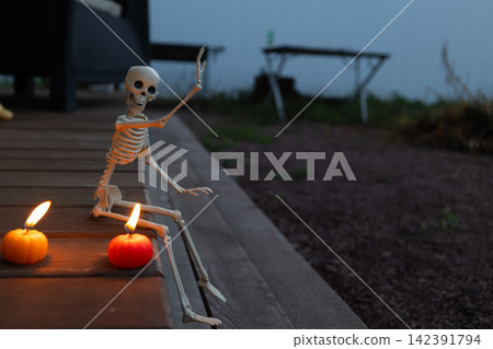 Candlelit Skeleton on Twilight Halloween Patio: Mystical Glow from Pumpkin Candles Candlelit Skeleton on Twilight Halloween Patio: Mystical Glow from Pumpkin Candles 142391794