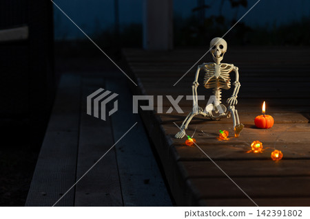 Halloween Night Glow: Skeleton Figurine on a Moonlit Deck with Candles and Glowing Pumpkins Halloween Night Glow: Skeleton Figurine on a Moonlit Deck with Candles and Glowing Pumpkins 142391802