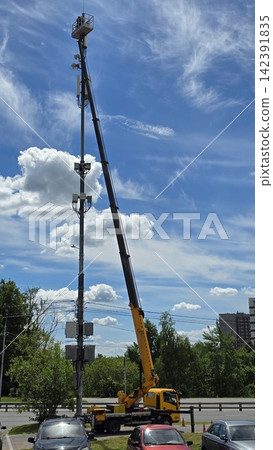 A mature male technician working on a cell tower mast using a yellow hydraulic crane truck in the city. A mature male technician working on a cell tower mast using a yellow hydraulic crane truck in the city. 142391835