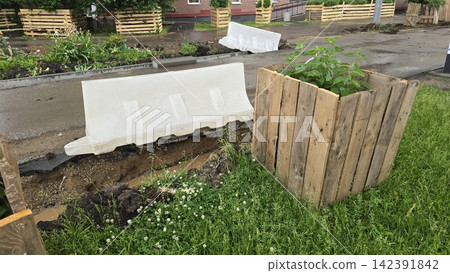 A construction site features wooden plant boxes and white plastic safety barriers near a dug city trench. A construction site features wooden plant boxes and white plastic safety barriers near a dug city trench. 142391842