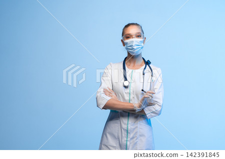 Medical worker wearing personal protective equipment, looking at camera and holding syringe on blue background Medical worker wearing personal protective equipment, looking at camera and holding syringe on blue background 142391845