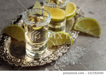 Tequila with salt and lime slices on a silver tray. Tequila with salt and lime slices on a silver tray. 142392040