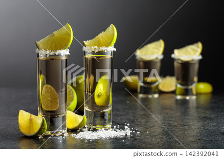 Tequila shots with salt and lime slices on a black stone table. Tequila shots with salt and lime slices on a black stone table. 142392041