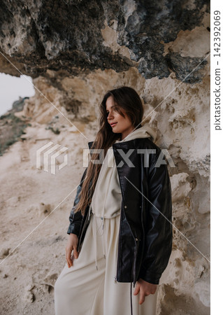 Woman leather jacket cliff posing under a rocky limestone overhang in stylish neutral casual wear at coastal landscape Woman leather jacket cliff posing under a rocky limestone overhang in stylish neutral casual wear at coastal landscape 142392069