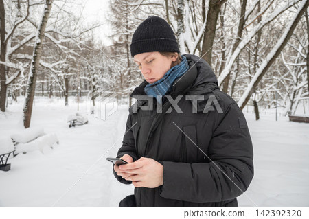 Young man using smartphone outdoors during winter snowfall Young man using smartphone outdoors during winter snowfall 142392320