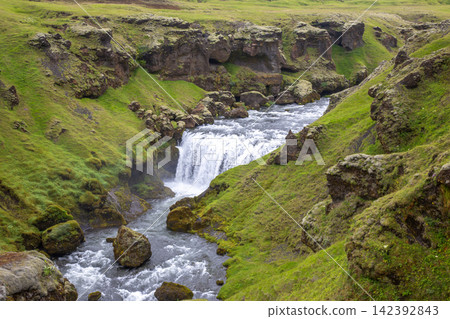Water flows through green hills and rocks in Iceland during daylight hours Water flows through green hills and rocks in Iceland during daylight hours 142392843