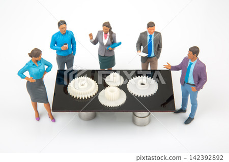 Miniature people discuss gears on a table in a bright room 142392892