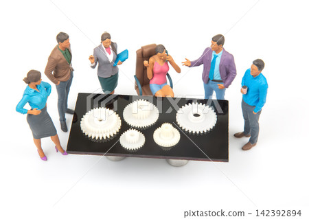 Miniature people gather around a table with gears discussing a project in a business setting Miniature people gather around a table with gears discussing a project in a business setting 142392894