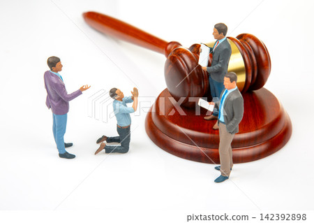 Miniature people gather around a gavel while engaging in various actions at a mock courtroom scene 142392898