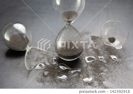 Sand flows from broken hourglass on dark surface Sand flows from broken hourglass on dark surface 142392918