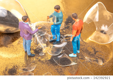 Miniature people examining broken glass pieces on a shiny surface Miniature people examining broken glass pieces on a shiny surface 142392921