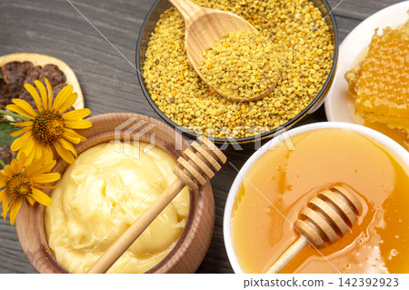 Various types of honey and bee products are arranged on a wooden table with flowers and a spoon Various types of honey and bee products are arranged on a wooden table with flowers and a spoon 142392923