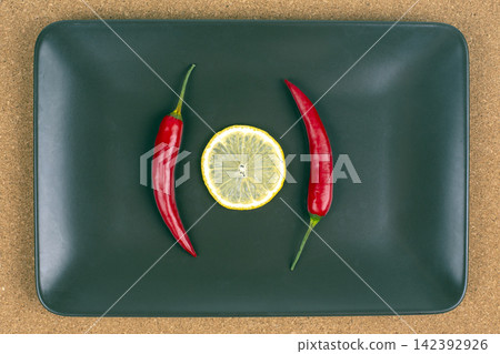 Fresh red chili peppers and lemon slice on a green plate in a kitchen setting Fresh red chili peppers and lemon slice on a green plate in a kitchen setting 142392926