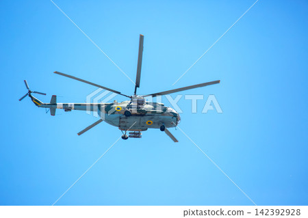Helicopter flies in clear sky over open area during sunny day Helicopter flies in clear sky over open area during sunny day 142392928