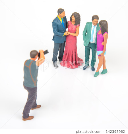 Miniature people gathered for a photo shoot with a photographer taking pictures at a simple backdrop Miniature people gathered for a photo shoot with a photographer taking pictures at a simple backdrop 142392962