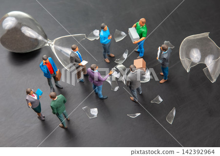 Miniature people gathered around broken hourglass on a dark surface during daytime Miniature people gathered around broken hourglass on a dark surface during daytime 142392964