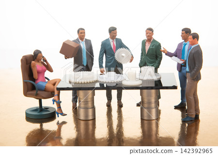 Miniature people having a meeting around a table with gears, in a bright setting during daytime 142392965