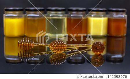 Different types of honey displayed in jars with honey dippers on a reflective surface Different types of honey displayed in jars with honey dippers on a reflective surface 142392976