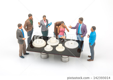 Miniature people in a meeting around a table with gears in a work setting Miniature people in a meeting around a table with gears in a work setting 142393014