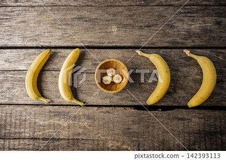 Four bananas and a bowl of slices on rustic wood Four bananas and a bowl of slices on rustic wood 142393113