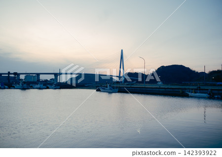 A cable-stayed bridge spanning the harbor at dusk and the calm sea. A cable-stayed bridge spanning the harbor at dusk and the calm sea. 142393922