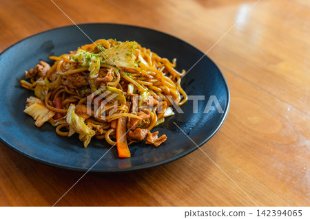 盛在黑色盤子裡的豬肉蔬菜炒麵,盤子放在木桌上。 盛在黑色盤子裡的豬肉蔬菜炒麵,盤子放在木桌上。 142394065