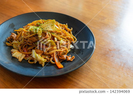 A generous portion of yakisoba noodles with plenty of toppings, placed on the right side of a wooden table. A generous portion of yakisoba noodles with plenty of toppings, placed on the right side of a wooden table. 142394069