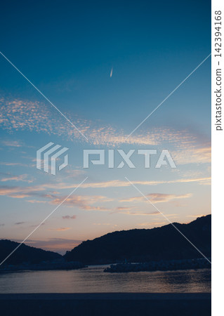 Contrails floating over the sea and mountain range at dusk. Contrails floating over the sea and mountain range at dusk. 142394168