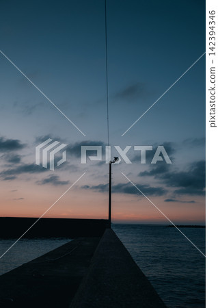 The sea at dusk and a single utility pole stretching along the breakwater. The sea at dusk and a single utility pole stretching along the breakwater. 142394346
