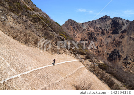 一名登山者正穿越栃木縣那須山山坡上的雪原,背景是旭山。 一名登山者正穿越栃木縣那須山山坡上的雪原,背景是旭山。 142394358