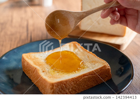 用木匙在吐司上塗抹蜂蜜 用木匙在吐司上塗抹蜂蜜 142394413