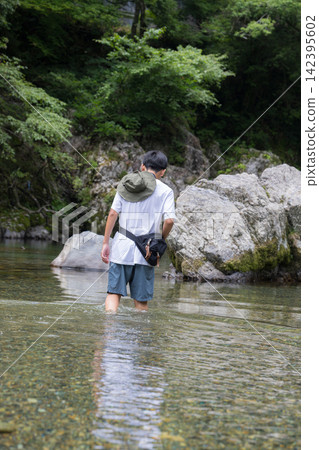一個男孩沿著清澈的夏日溪流散步，享受著大自然的美麗；溪水嬉戲和戶外美景。 142395602