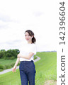 A woman strolling through a grassland or riverbank. 142396604