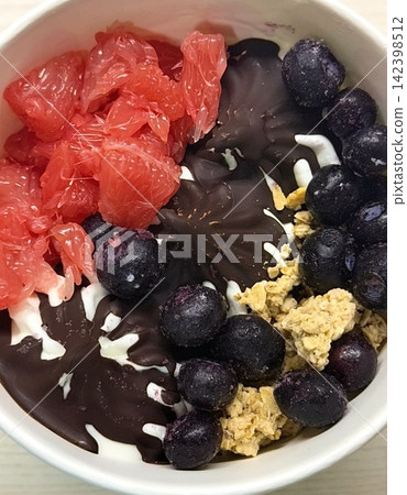 Swirled yogurt ice cream dessert served in a cup, smooth creamy texture with glossy surface, topped with fresh fruit pieces, highlighting its refreshing and inviting appearance in detail 142398512