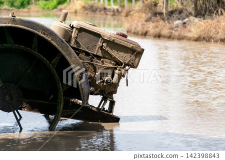 Mud covered walking tractor working flooded rice field during soil preparation for rice cultivation traditional agricultural farming Mud covered walking tractor working flooded rice field during soil preparation for rice cultivation traditional agricultural farming 142398843