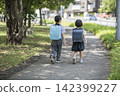 The backs of children, still wearing their school bags, walking in a line along the school route. 142399227