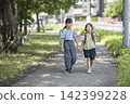 Elementary school students, wearing their school bags, walk side by side along their route to school. 142399228