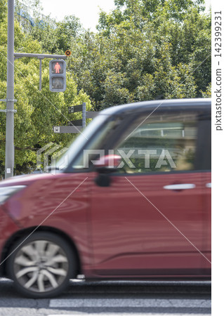 A red car driving across a pedestrian crossing 142399231