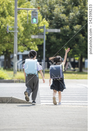 The backs of children in school backpacks crossing a pedestrian crossing. 142399233