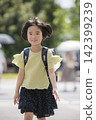 A smiling elementary school student walking with a schoolbag on her back. 142399239