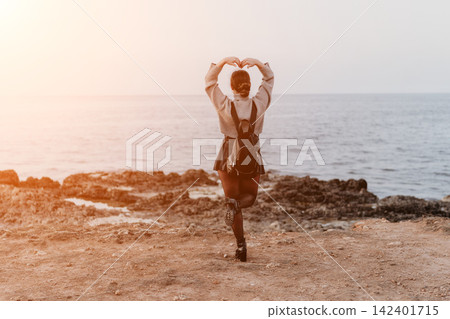 Woman sunset ocean heart shape hand gesture by young traveler on rocky coast during peaceful golden hour evening Woman sunset ocean heart shape hand gesture by young traveler on rocky coast during peaceful golden hour evening 142401715